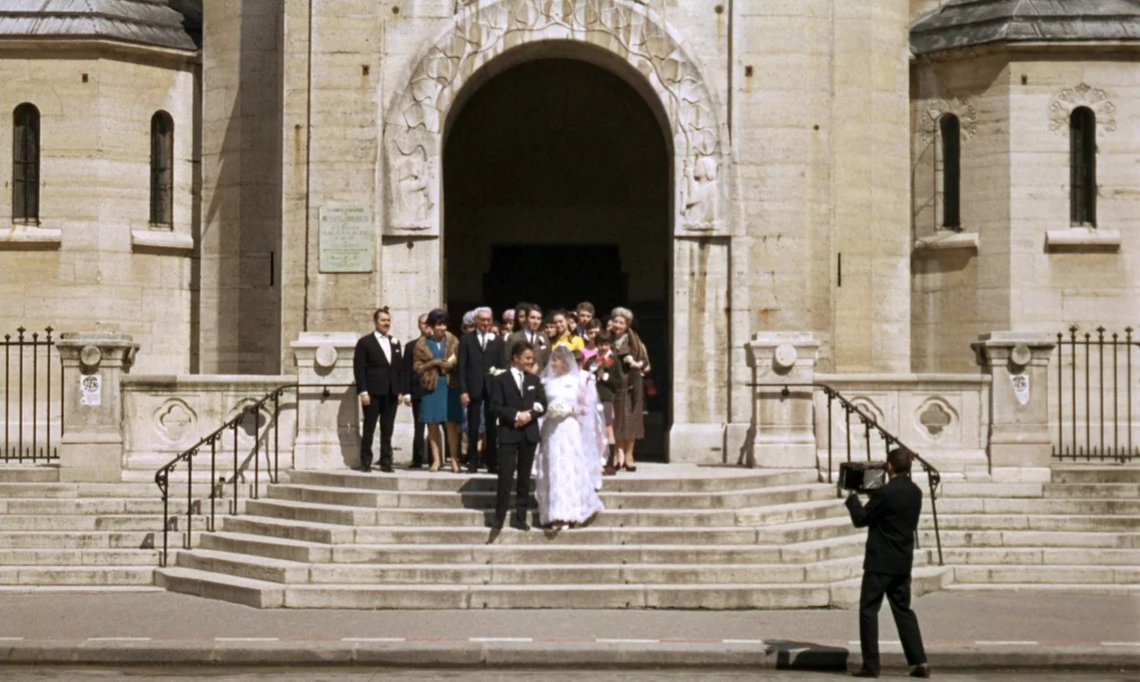 The Bride Wore Black (1968) movie still: wide — A stone church entrance with a large arched door stands above a wide staircase. A wedding party…