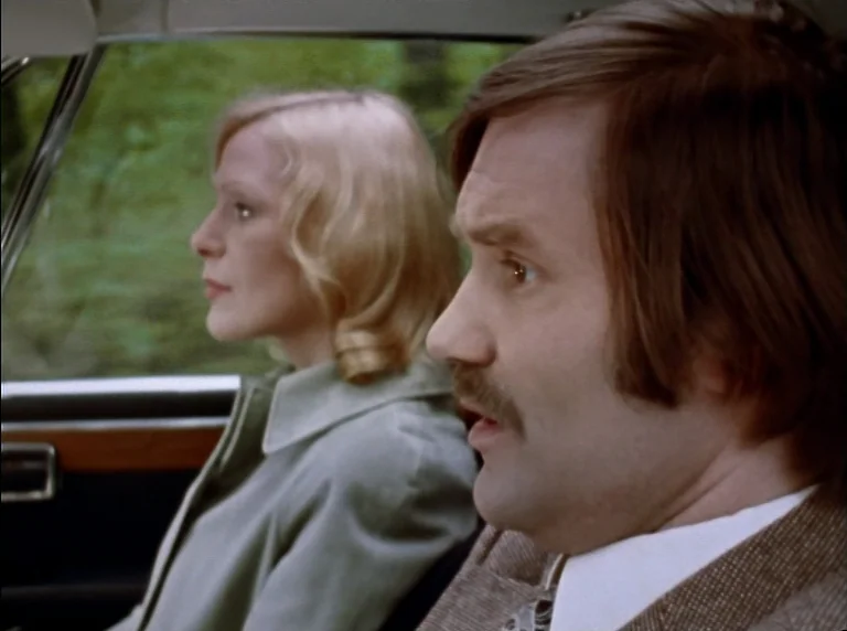 Fear Of Fear (1975) movie still: medium — The interior of a moving 1970s sedan features wood grain dashboard trim. A man with a mustache and a…