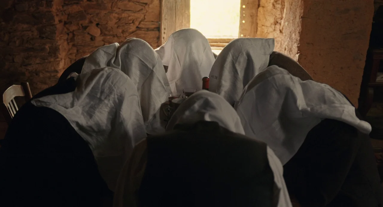 The Taste of Things (2023) movie still: medium — A stone-walled interior space features a table surrounded by figures draped in white cloths. The…
