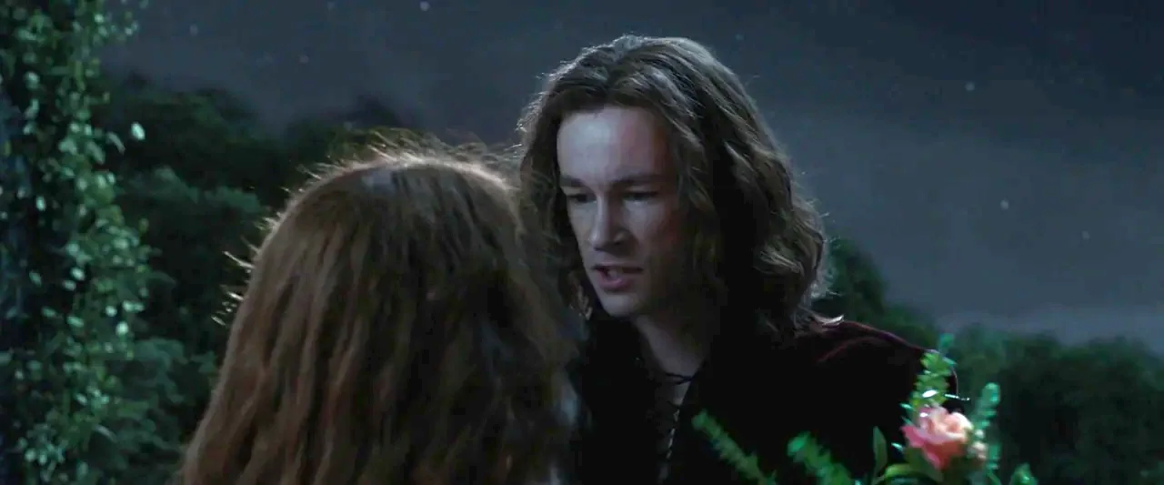 Rosaline (2022) movie still: medium — A night landscape features a dimly lit grassy area under a starry sky. A man with long brown hair looks at an…