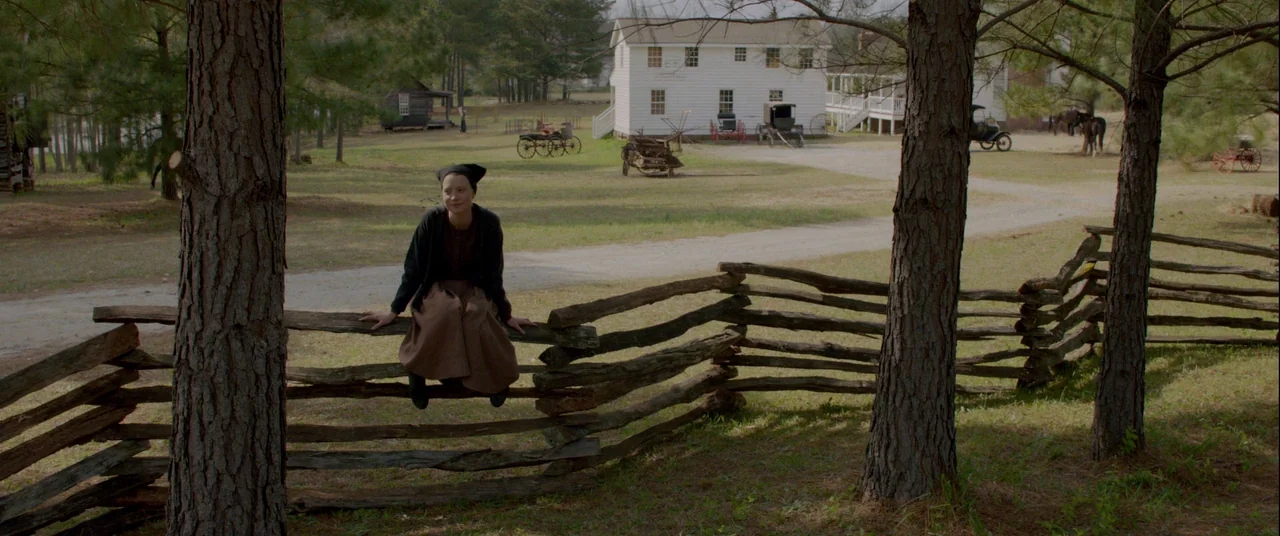 Lawless (2012) movie still: wide — A rural settlement features a white wooden house and old farming equipment on dirt. A woman sits on a rustic…