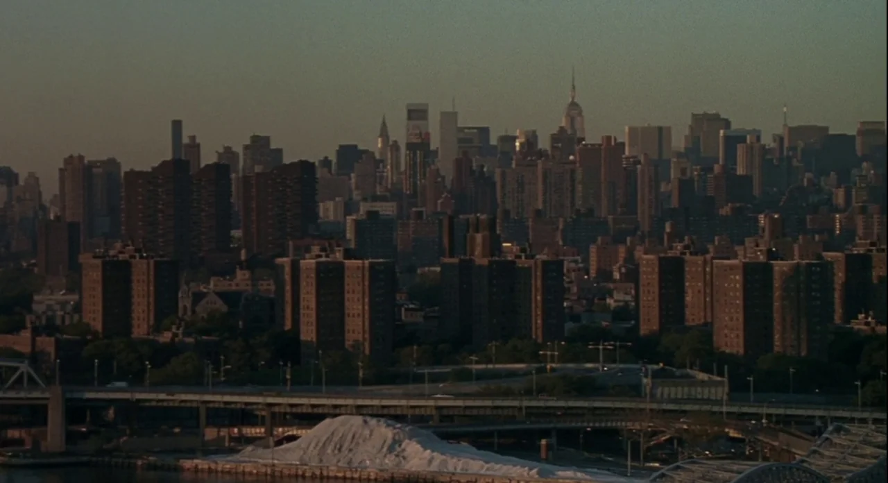 American Gangster (2007) movie still: establishing — A dense urban landscape with numerous apartment blocks and high-rises under a dim sky. An…