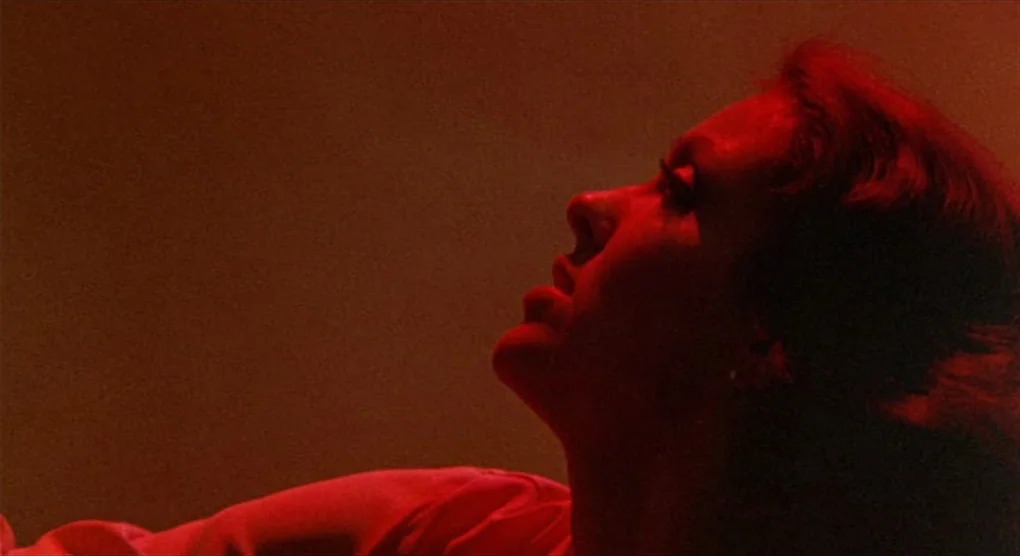All That Jazz (1979) movie still: closeup — The frame shows a close view of a person bathed in intense red light. A woman's profile is visible as…