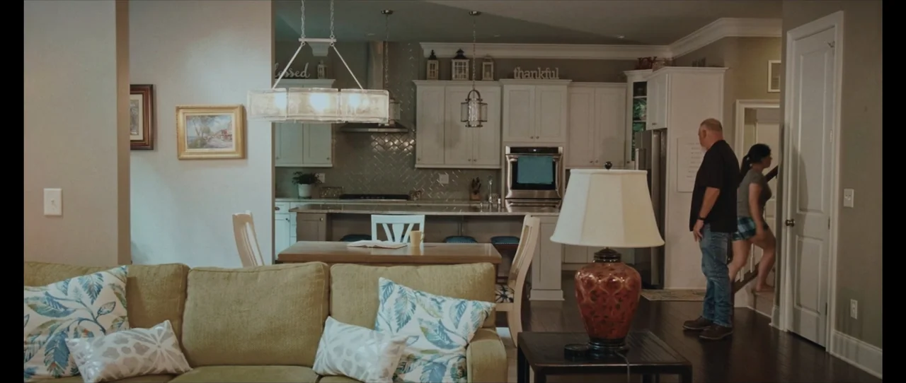 Ordinary Things (2001) movie still: wide — A spacious home interior features an open-plan living room connected to a modern kitchen. A bald man…