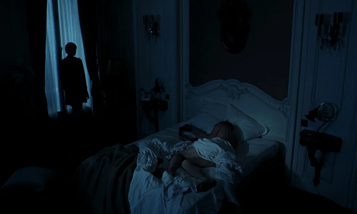 Daughters of Darkness (1971) movie still: wide — A dimly lit room with classic wall moldings and a large bed. A silhouette stands by the window…