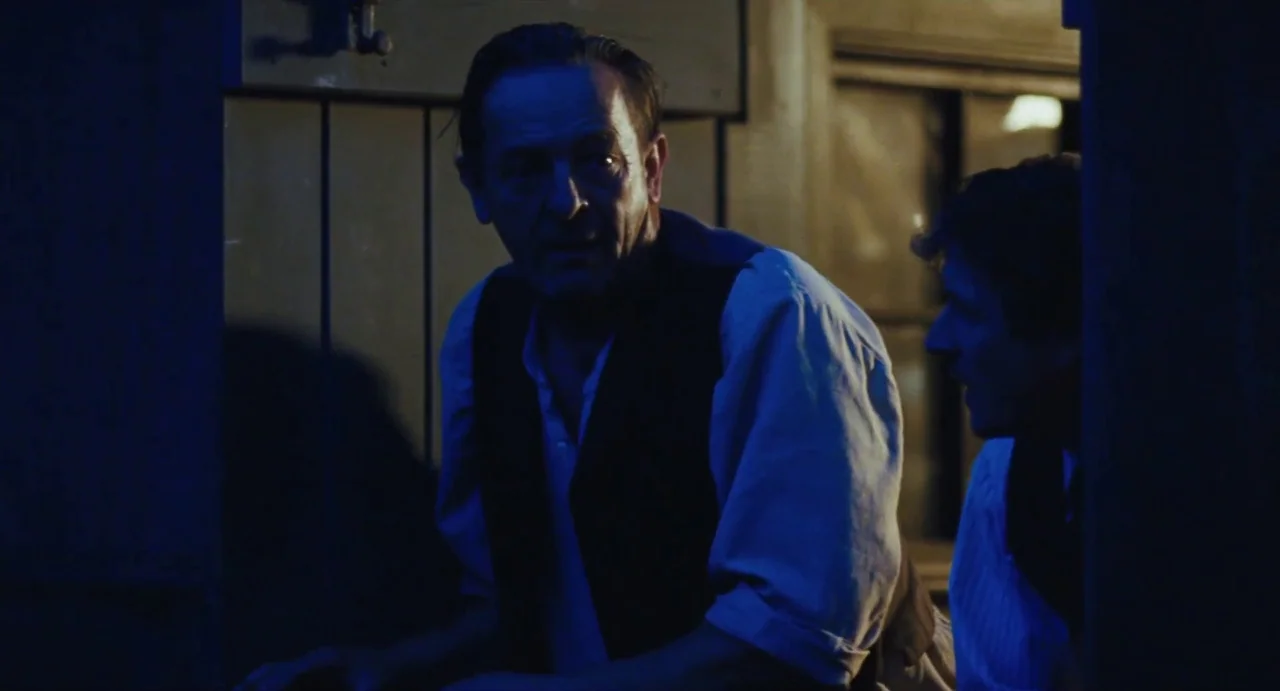 Jimmy’s Hall (2014) movie still: medium — Two men stand within a wooden doorway in a dark, dimly lit environment. They gaze outward into the…