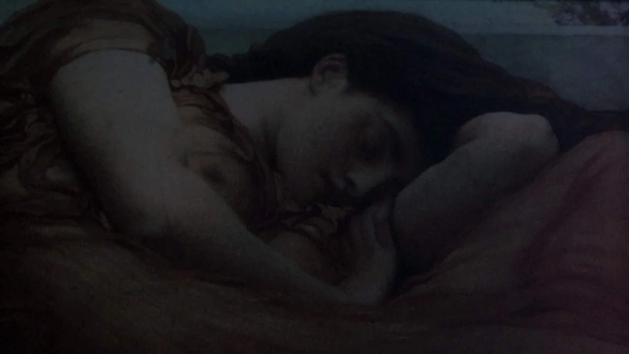 Picnic at Hanging Rock (1975) movie still: closeup — A dimly lit indoor space featuring a person resting on a fabric surface. The subject is asleep…