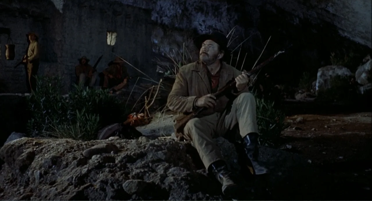 Chato's Land (1972) movie still: medium — A dark, rocky cave interior serves as a makeshift camp for several armed men. The primary subject sits on…