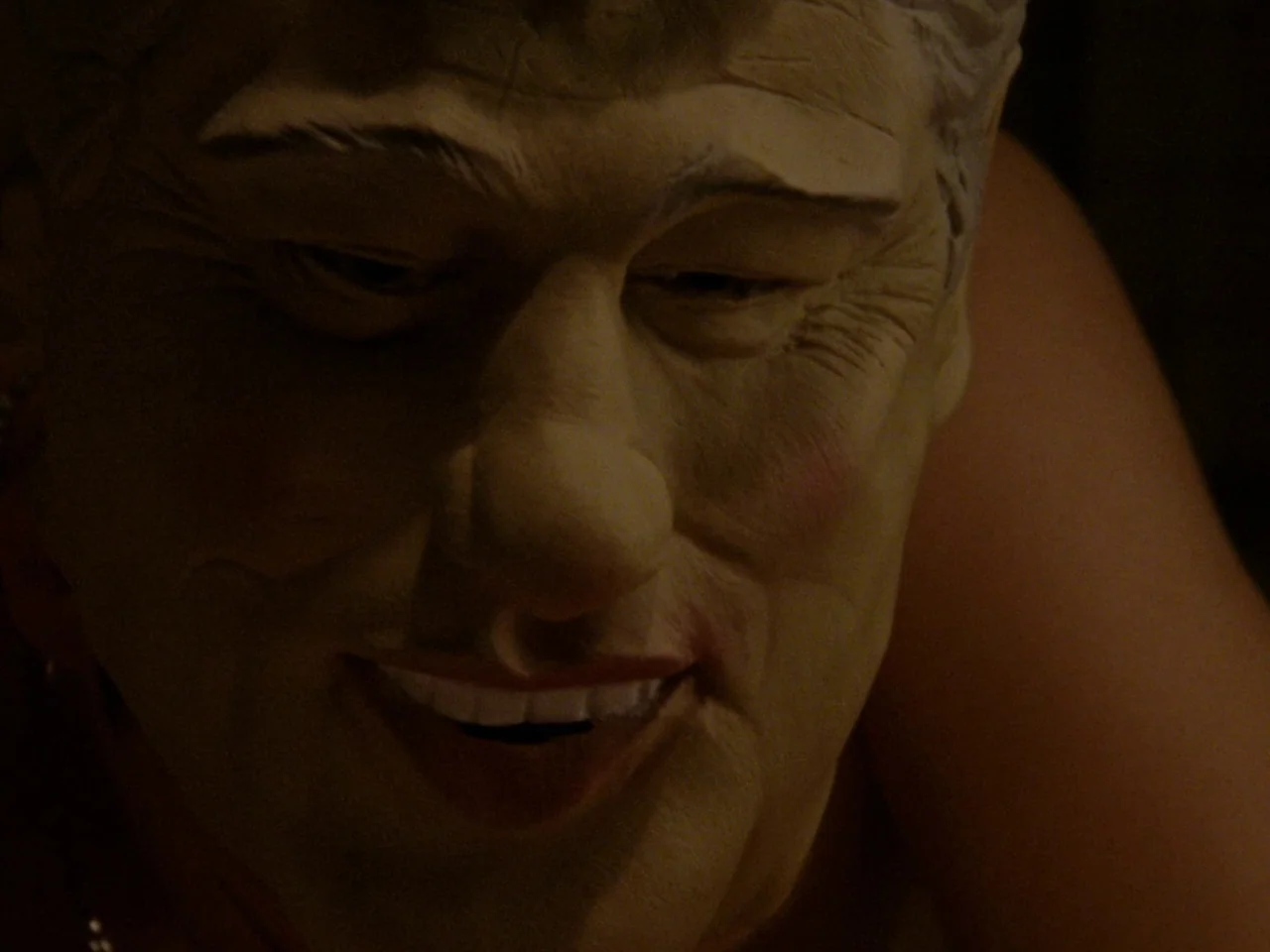 Mid90s (2018) movie still: closeup — An interior space is dimly lit in the darkness of night. A person wears a Bill Clinton rubber mask that…