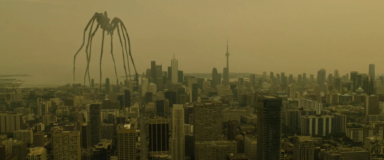 Enemy (2013) movie still: establishing — A dense urban cityscape is covered by a persistent, heavy yellow atmospheric haze. A gargantuan spider-like…
