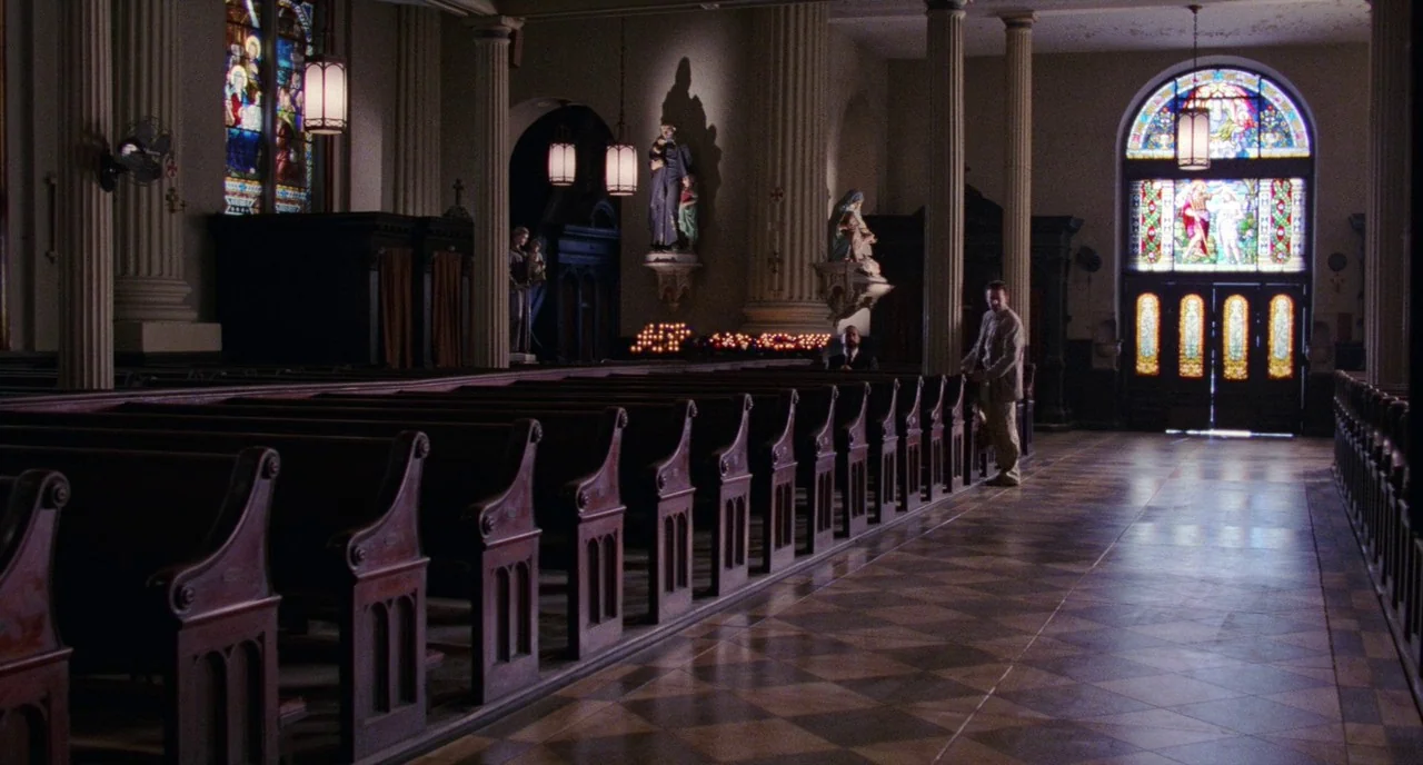 Angel Heart (1987) movie still: wide — A quiet church interior features rows of dark wooden pews and stone columns. A lone man stands near the…