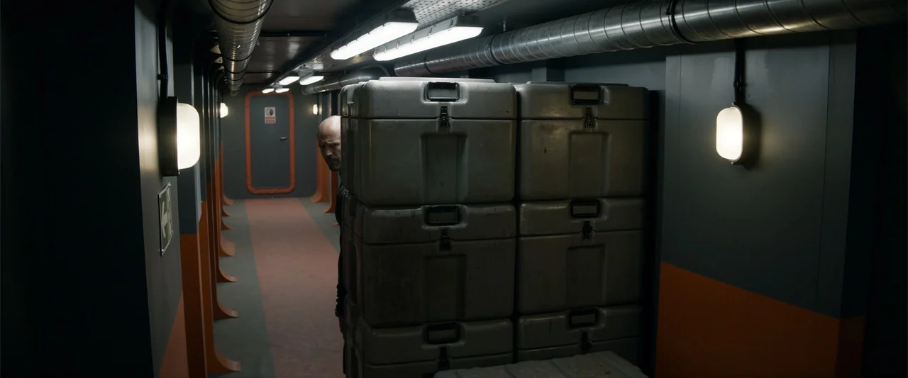 Meg 2: The Trench (2023) movie still: medium — An industrial-looking narrow corridor features grey walls with orange bands and overhead ventilation…