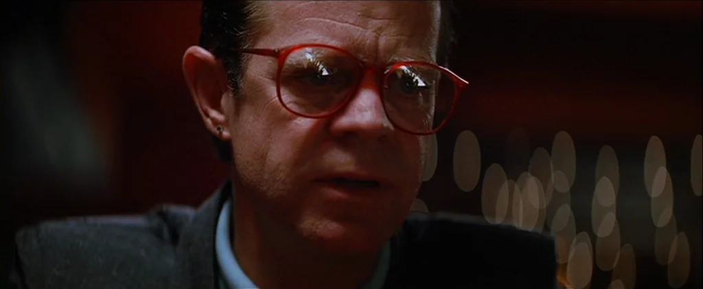 Magnolia (1999) movie still: closeup — A man sits in a dimly lit setting with bokeh lights visible on the right. He stares slightly past the lens…