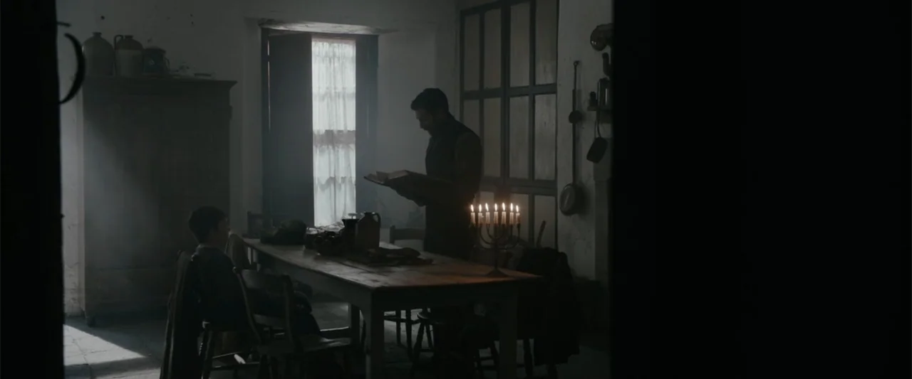 Freud's Last Session (2023) movie still: medium — A dimly lit room features a long wooden table with a silver candelabra centerpiece. A man reads…