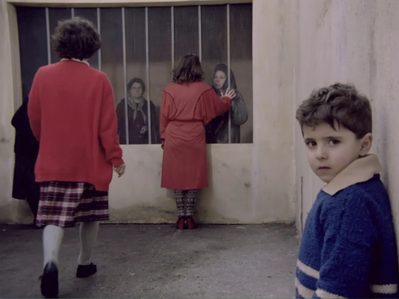Don't Let Them Shoot the Kite (1989) movie still: wide — A concrete enclosure features a metal-barred window dividing two separate areas. A young…