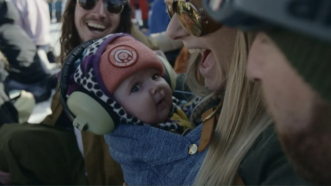 Dear Rider: The Jake Burton Story (2021) movie still: closeup — A snowy outdoor environment at a ski resort features several people in winter…