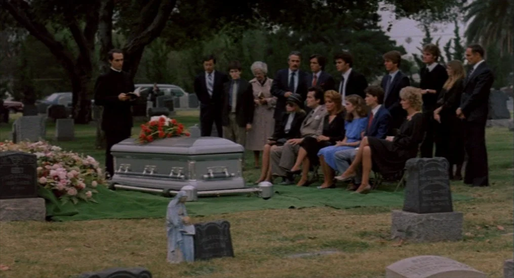 A Nightmare On Elm Street (1984) movie still: wide — A group of people in formal attire gather at a grave for a funeral. A priest stands at the head…