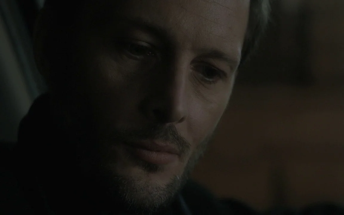 Let The Sunshine In (2017) movie still: closeup — A dark vehicle interior provides minimal ambient light on the driver's face. The man looks down…