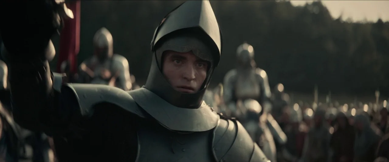The King movie still: medium — A field filled with soldiers in medieval armor stands beneath an overcast sky. A knight in the foreground looks…