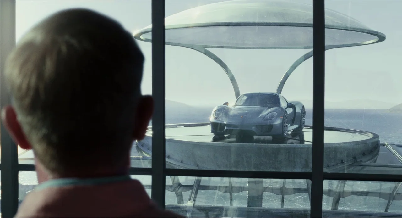 Glass Onion (2022) movie still: medium — A man looks through large glass windows at a modern structure over water. A silver sports car sits on a…