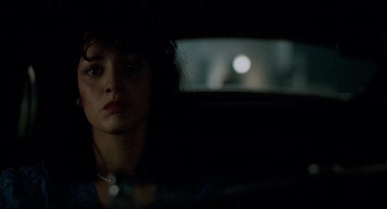 Devil In A Blue Dress (1995) movie still: closeup — A dark vehicle interior with a woman sitting in the passenger seat at night. A bright circular…