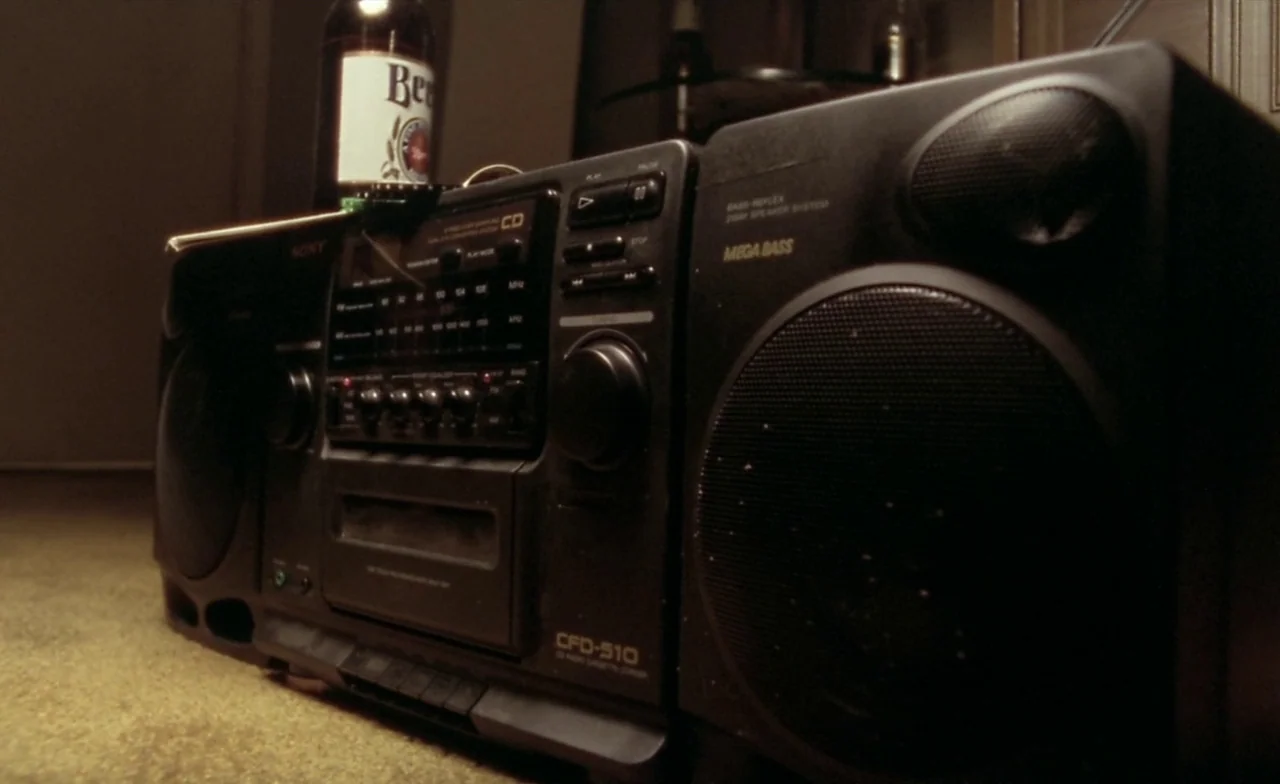 Leaving Las Vegas (1995) movie still: closeup — A black plastic Sony boombox sits on a carpeted floor in a dim room. A glass bottle rests directly…