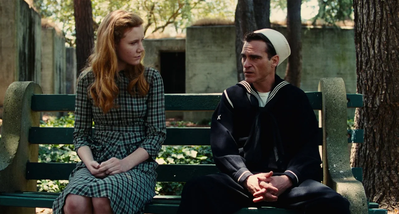 The Master (2012) movie still: medium — A park setting features a dark green wooden bench placed against concrete landscape structures. A woman in a…