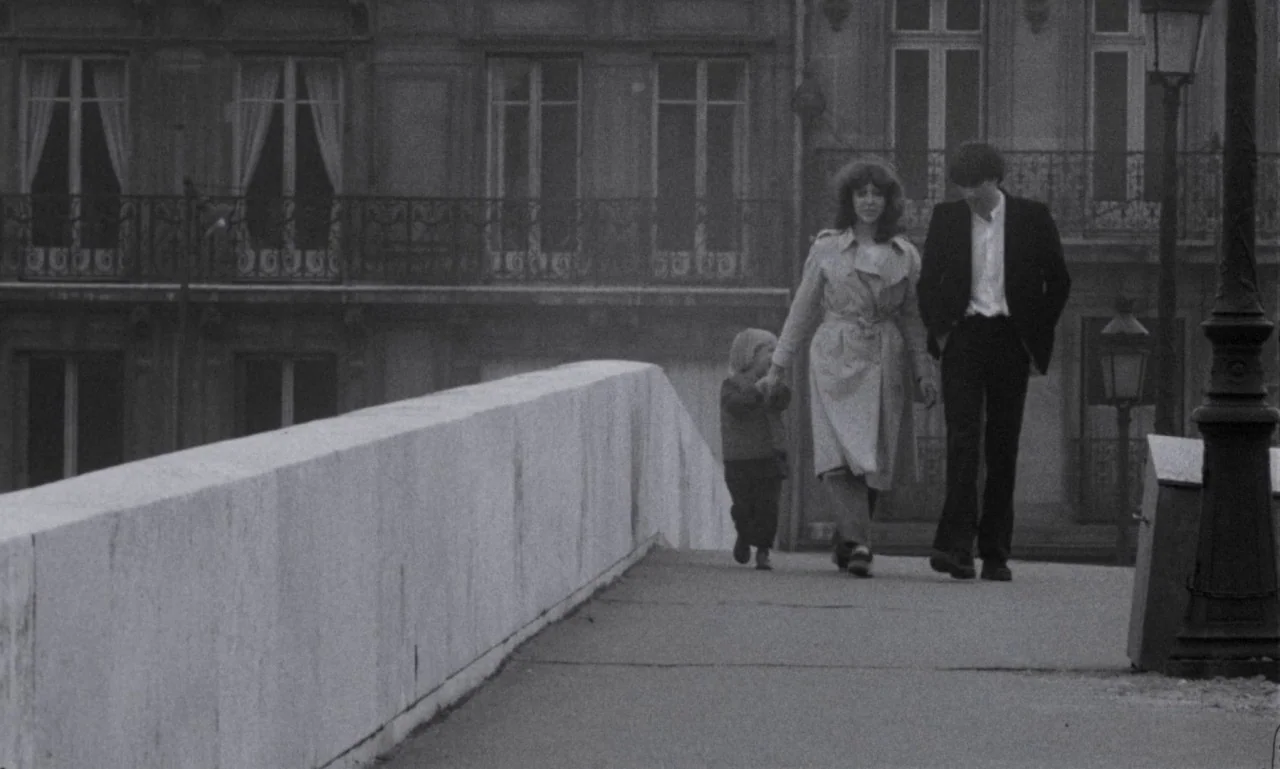 The Secret Son (1979) movie still: fullbody — A wide stone bridge stands before a series of multi-story European buildings with balconies. A man and…
