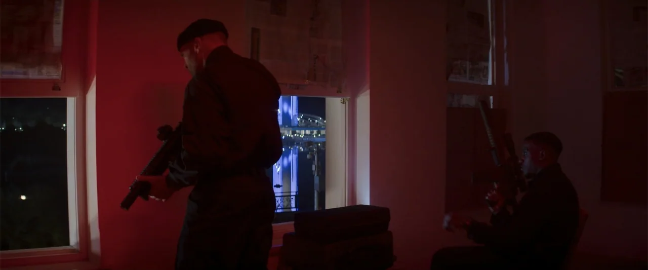 Operation Fortune: Ruse de Guerre (2023) movie still: fullbody — An interior room with white walls is illuminated by intense red exterior neon…
