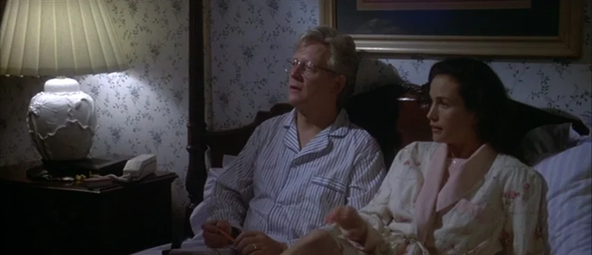 Short Cuts (1993) movie still: medium — A traditional bedroom interior features blue floral wallpaper and a dark wood headboard frame. A middle-aged…