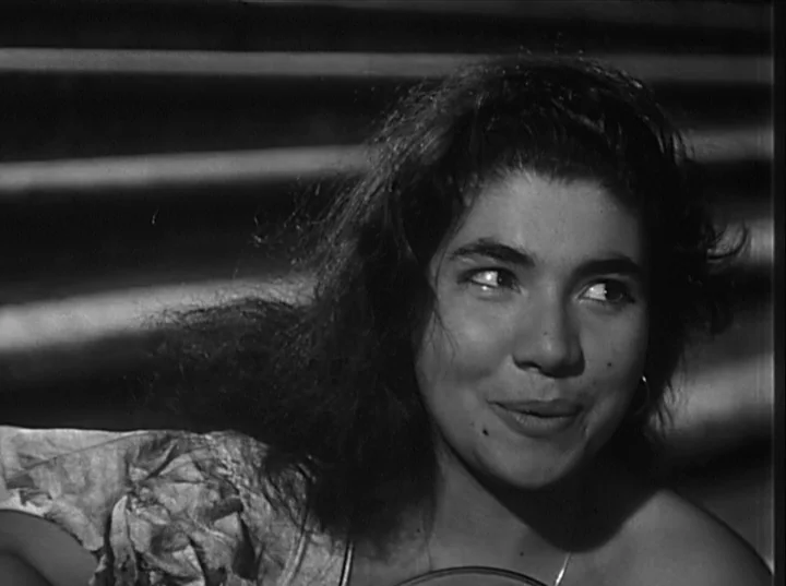 Variety Lights (1950) movie still: closeup — A close-up of a woman outdoors with horizontal metal tiers visible behind her. She turns her head and…