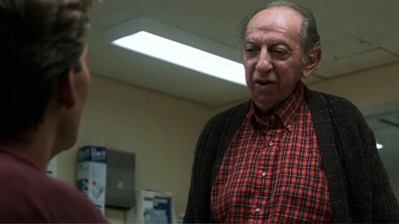 Ghost (1990) movie still: medium — A utilitarian office space with drop ceilings and beige walls shows a man talking. An elderly man with thinning…