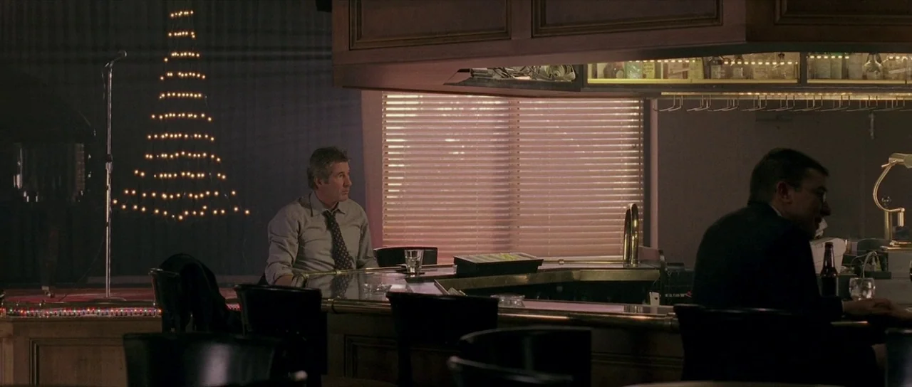 The Mothman Prophecies (2002) movie still: wide — A dimly lit lounge with wooden bar fixtures and a decorative light structure. Two men sit at the…