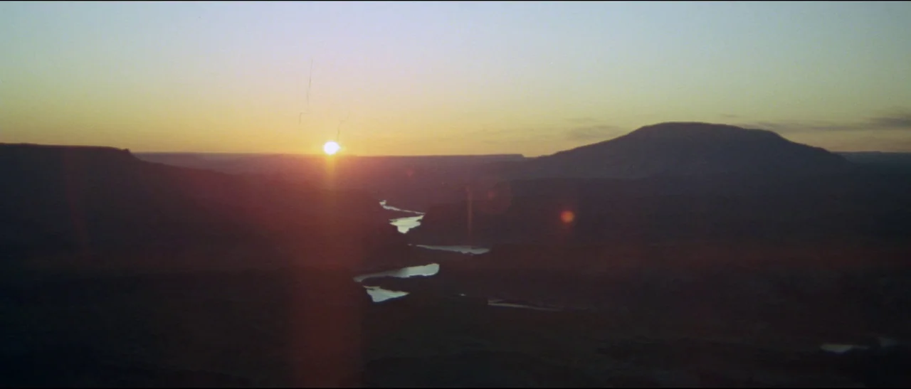 Planet of the Apes (1968) (1968) movie still: establishing — A vast canyon landscape is viewed at sunrise with a winding river below. The sun sits…