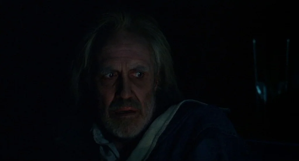 Melvin & Howard (1980) movie still: closeup — An older man is positioned in a dark, nondescript interior space. He gazes off-camera toward an unseen…