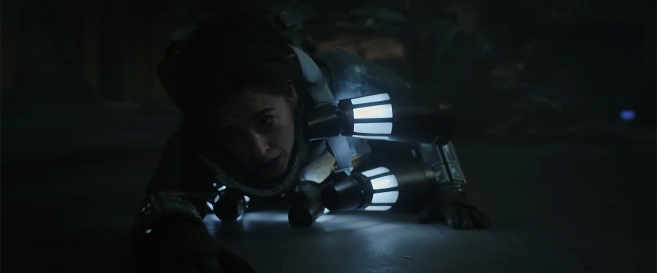 DISTANT (2026) movie still: medium — A dark, metallic interior floor provides the setting for a person in mechanical gear. A person crawls forward…