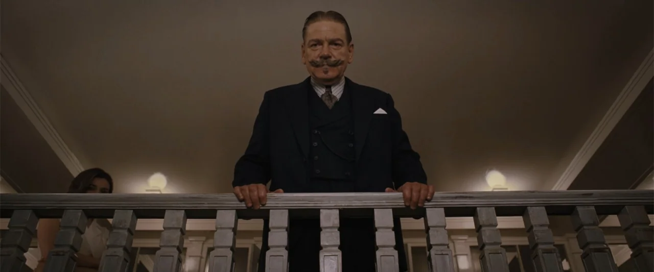 Death on the Nile (2022) movie still: medium — A man stands on a wooden balcony overlooking a dimly lit interior space. He looks down from behind…