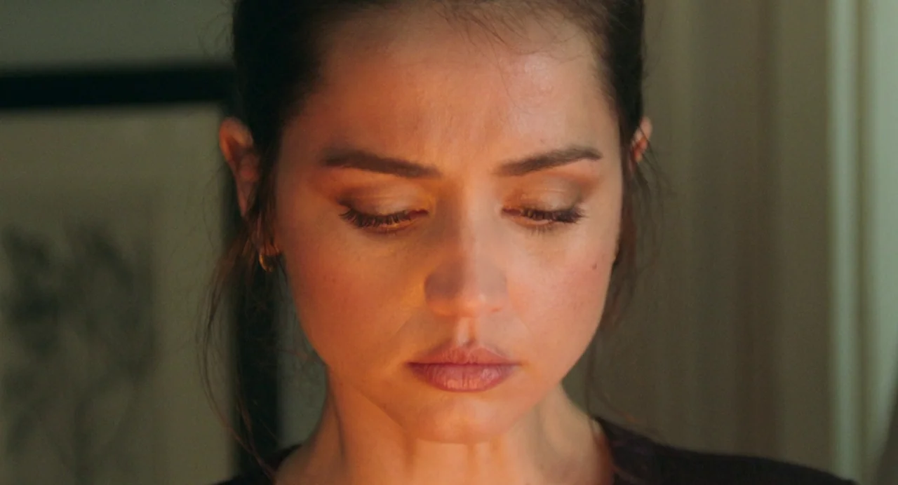 Deep Water (2022) movie still: closeup — A close-up shot focuses on a woman's face within an indoor setting. She gazes downward with her eyes…