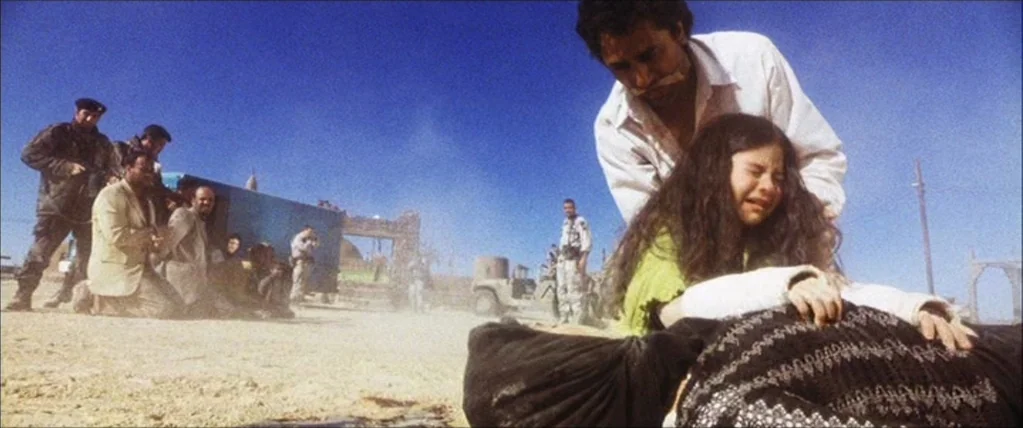 Three Kings (1999) movie still: medium — An arid, sun-baked landscape stretches out under a clear, bright blue sky. A young girl cries while a man…