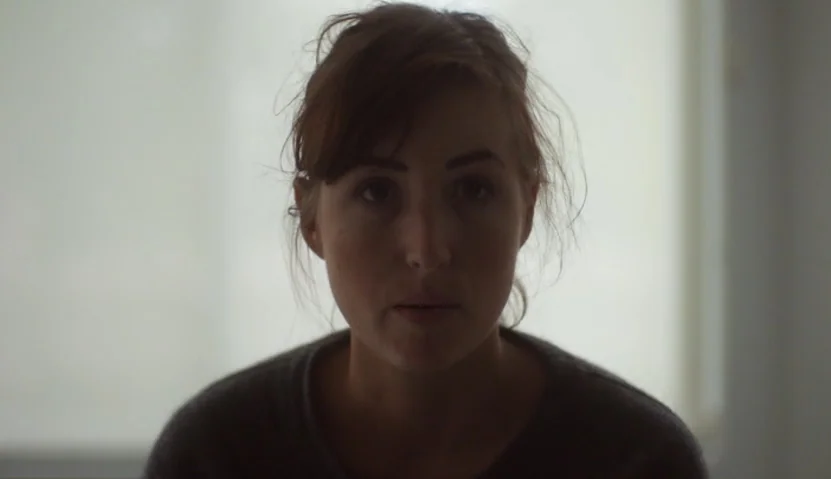 Kate Plays Christine (2016) movie still: closeup — A person stands centered before a bright, out-of-focus window in an indoor space. The subject…