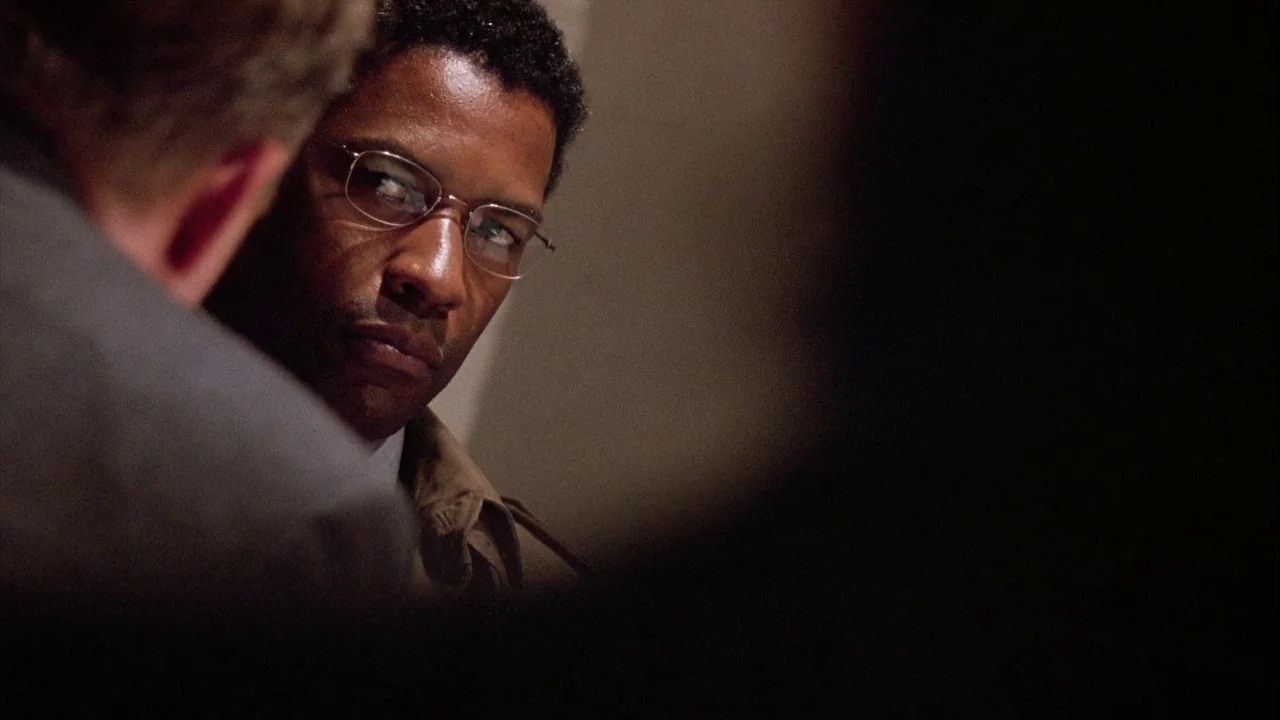 The Manchurian Candidate (2004) movie still: closeup — A dimly lit interior space features two individuals in close proximity. A man in glasses is…