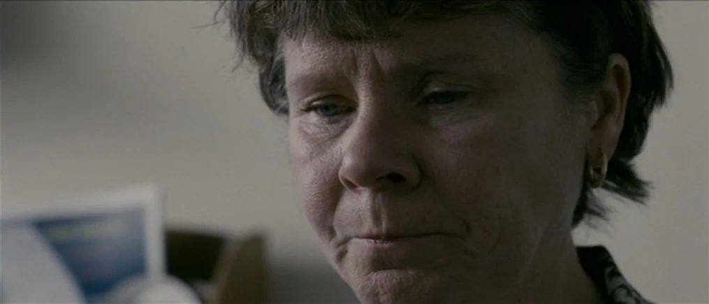 Another Year (2010) movie still: closeup — A plain interior room with a soft out-of-focus background. A mature woman with short brown hair looks…