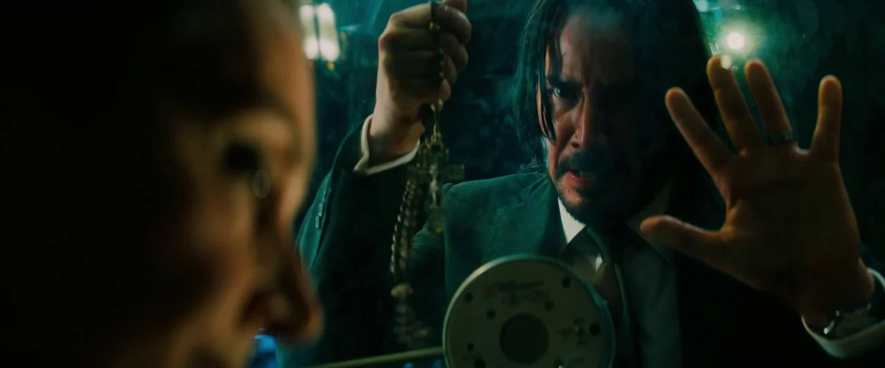 John Wick: Chapter 3 – Parabellum (2019) movie still: medium — A dimly lit visiting room features a thick glass partition separating two people. A…