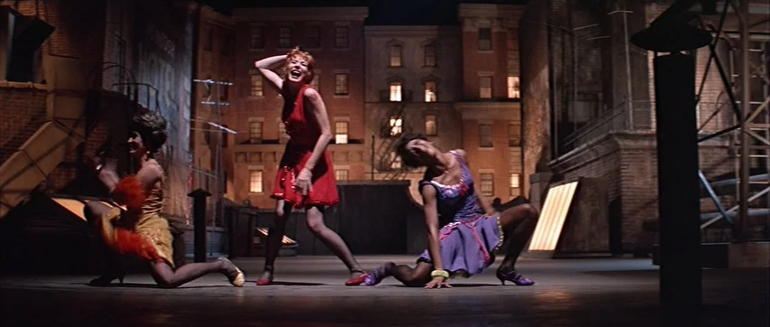 Sweet Charity (1969) movie still: fullbody — A dark urban rooftop set features brick buildings with illuminated windows in the distance. Three women…