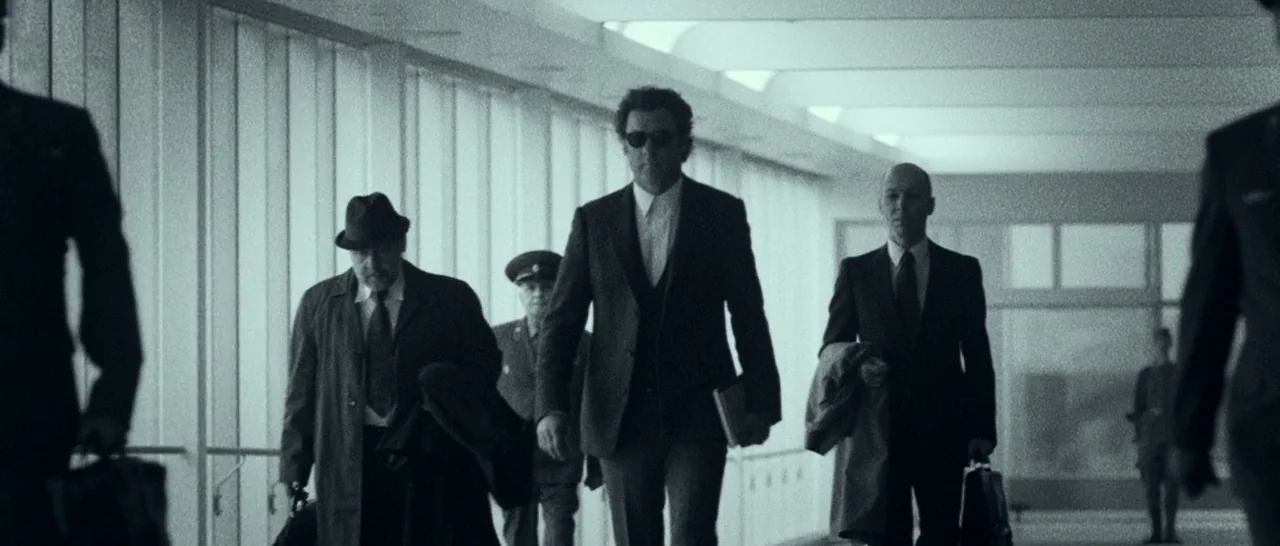 Pawn Sacrifice (2014) movie still: fullbody — A long, bright airport walkway with floor-to-ceiling glass panels and sterile white ceiling lights.…