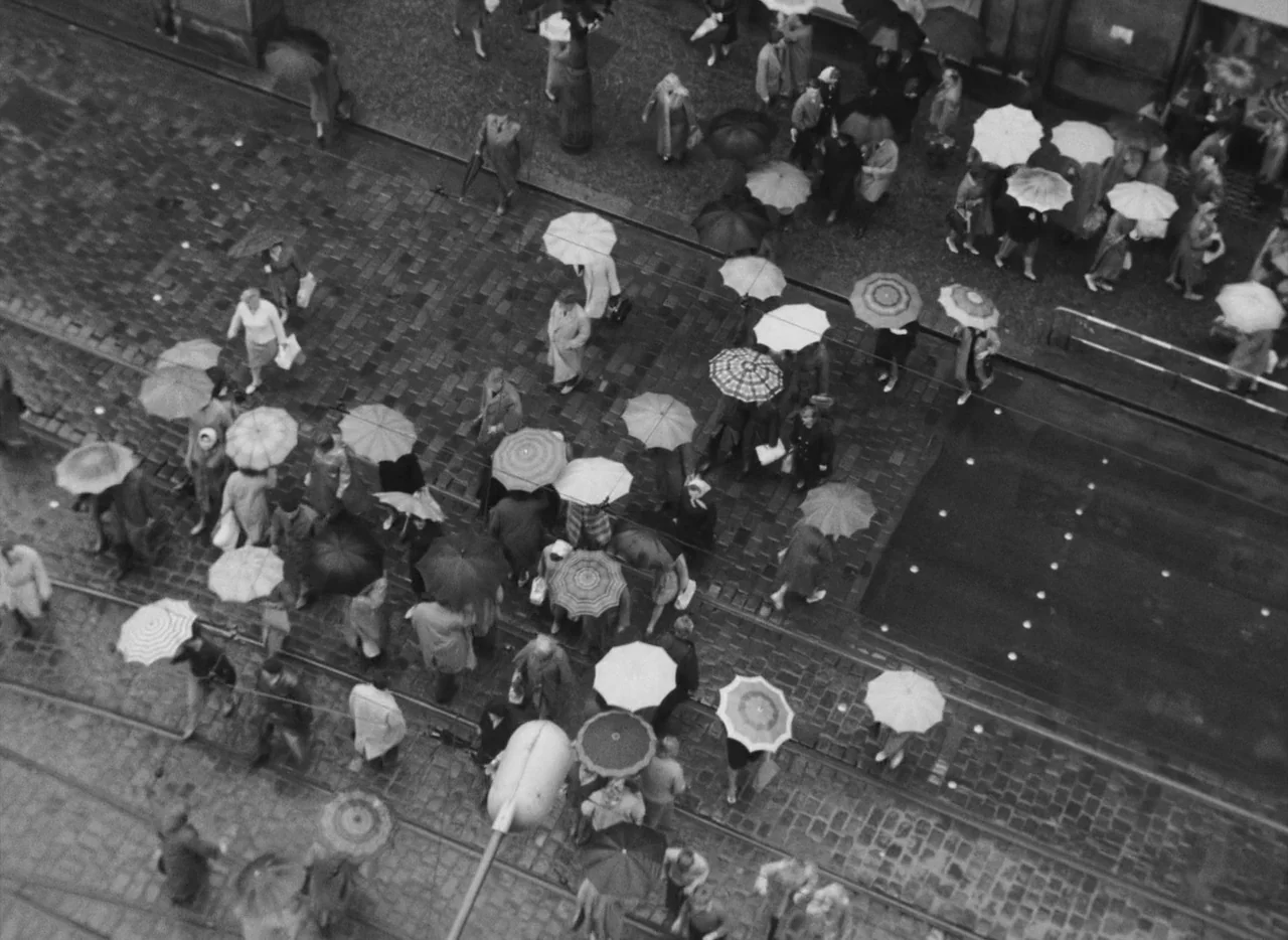 Pearls of the Deep (1965) movie still: wide — A wet cobblestone city street seen from a high-angle perspective with tram tracks visible. Many people…