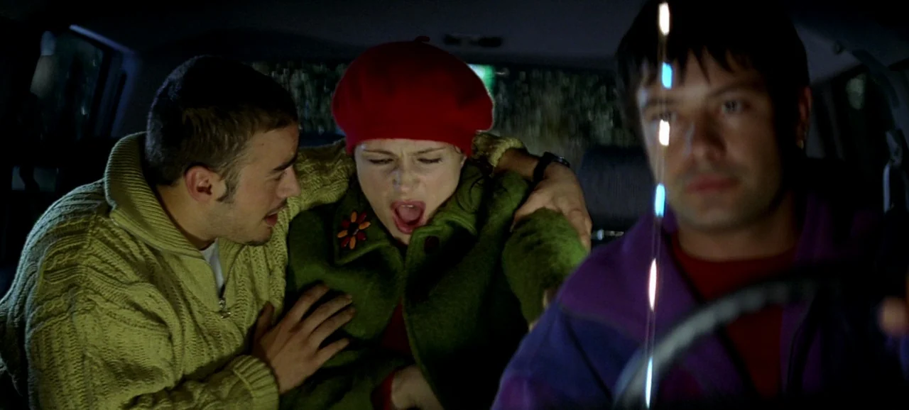 Live Flesh (1997) movie still: medium — The interior of a moving vehicle at night with three passengers. A man leans forward to console a woman who…