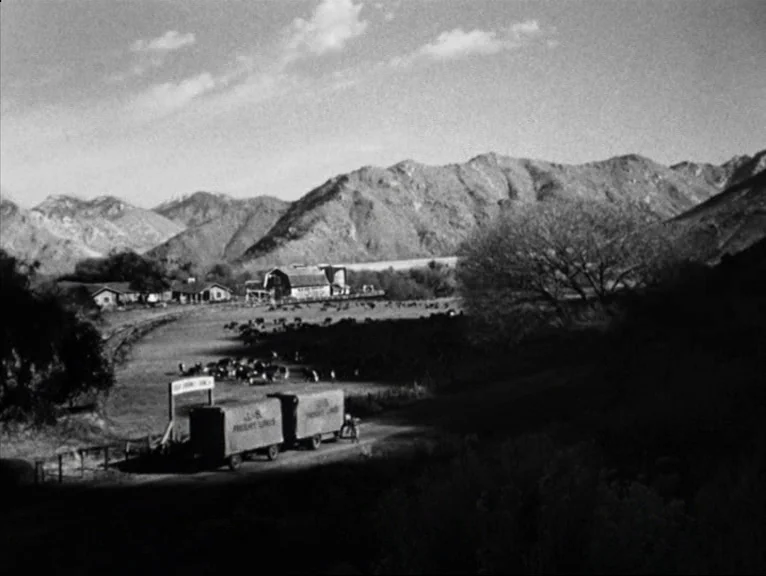 Saboteur (1942) movie still: wide — A rural valley features a ranch complex with barns and a nearby pasture. Cattle graze on the land near large…