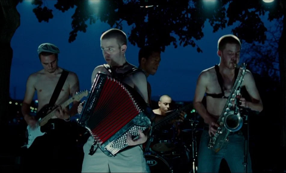 Hadewijch (2009) movie still: fullbody — A group of shirtless men play instruments under dark trees at night. They stand in a line playing guitar,…