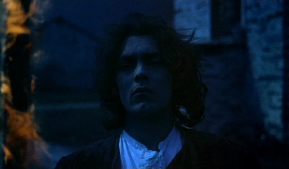 Heart of Glass (1976) movie still: medium — A man stands outdoors at night illuminated by the light of a nearby flame. The dark environment is…